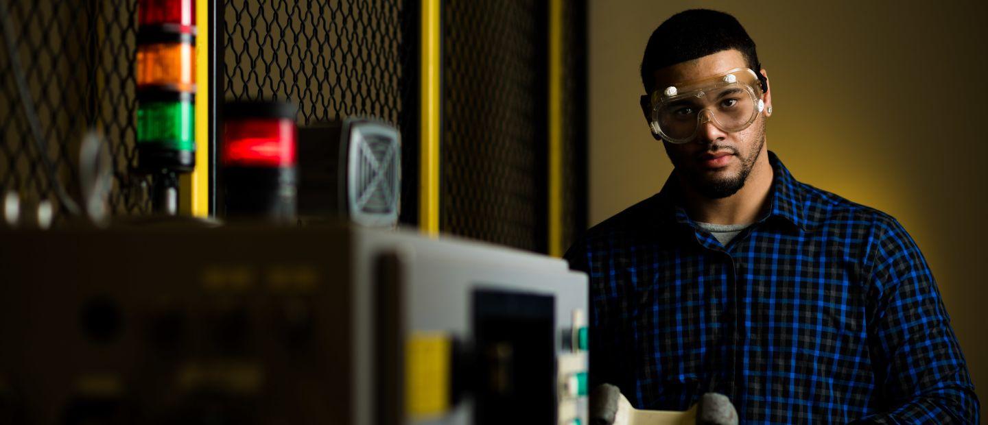 A man wearing safety goggles around mechanical equipment.